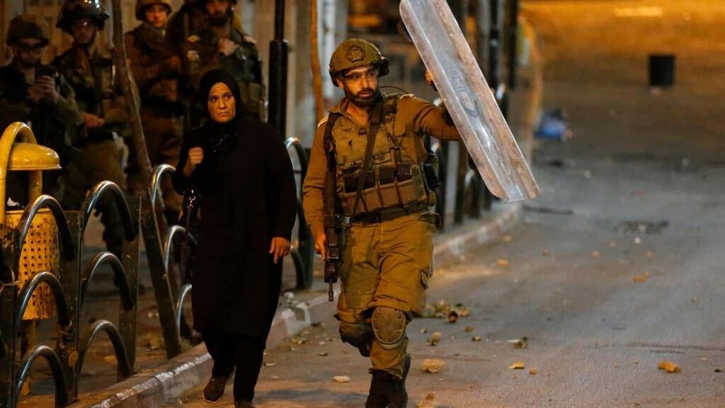 IDF officer protects Palestinian woman from stones in Hebron during clashes (Photo: Hebron) IDF officer protects Palestinian woman from stones in Hebron during clashes on Saturday
