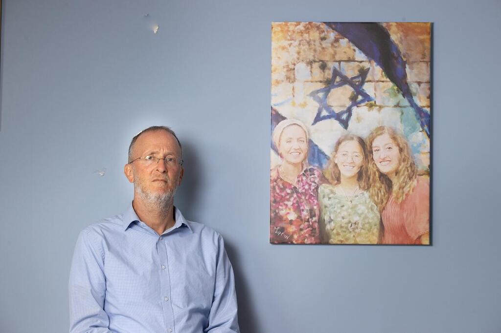 Rabbi Leo Dee stands beside a portrait of his late wife Lucy and daughters Maia and Rina, who were murdered in a terrorist attack in April 2023 (Photo: Alex Kolomoisky) הרב ליאו די