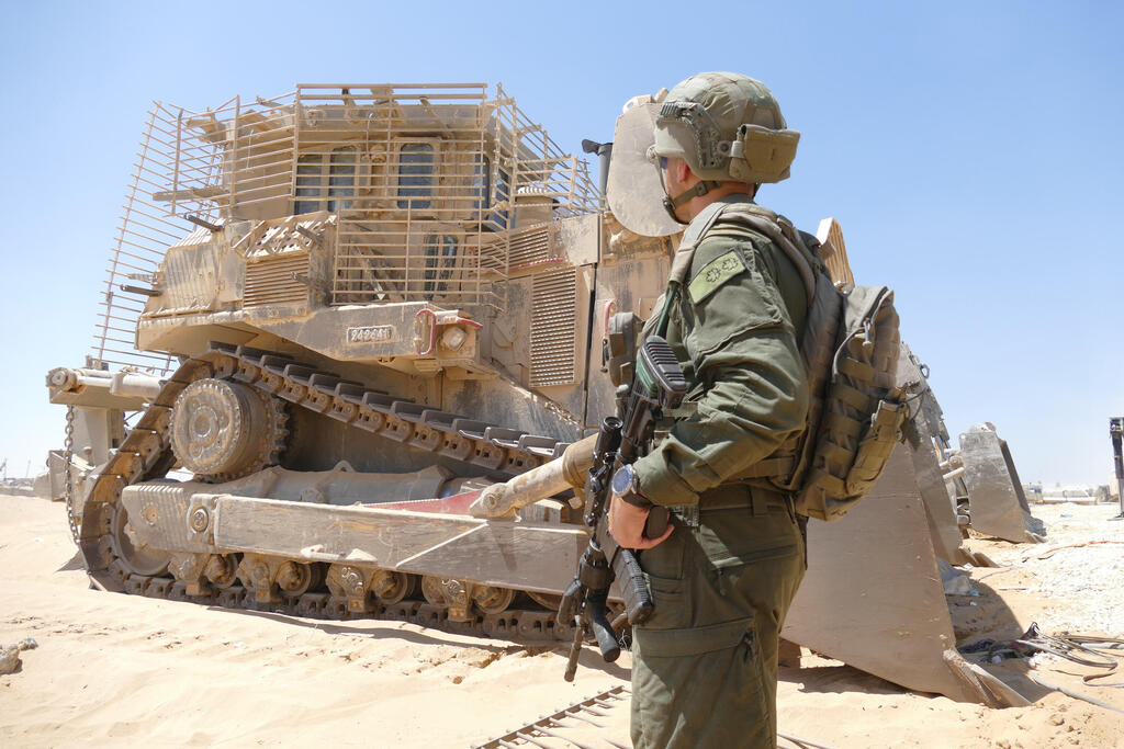 A soldier stands in front of a D9 bulldozer 