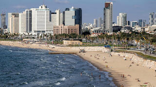 אנשים משתזפים ומשתכשכים במימי הים התיכון לאורך חוף הים בתל אביב