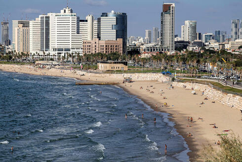 אנשים משתזפים ומשתכשכים במימי הים התיכון לאורך חוף הים בתל אביב