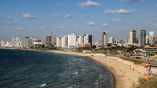 אנשים משתזפים ומשתכשכים במימי הים התיכון לאורך חוף הים בתל אביב