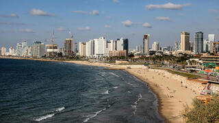 אנשים משתזפים ומשתכשכים במימי הים התיכון לאורך חוף הים בתל אביב