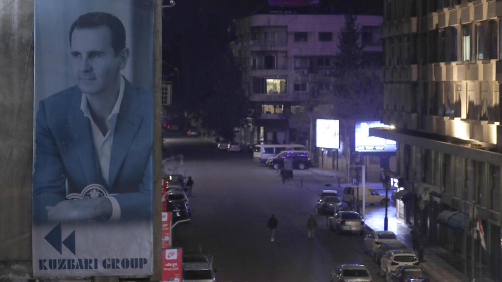 A giant banner of Syrian President Bashar Assad hangs on the facade of a building, as pedestrian walk through an the empty streets of Damascus
