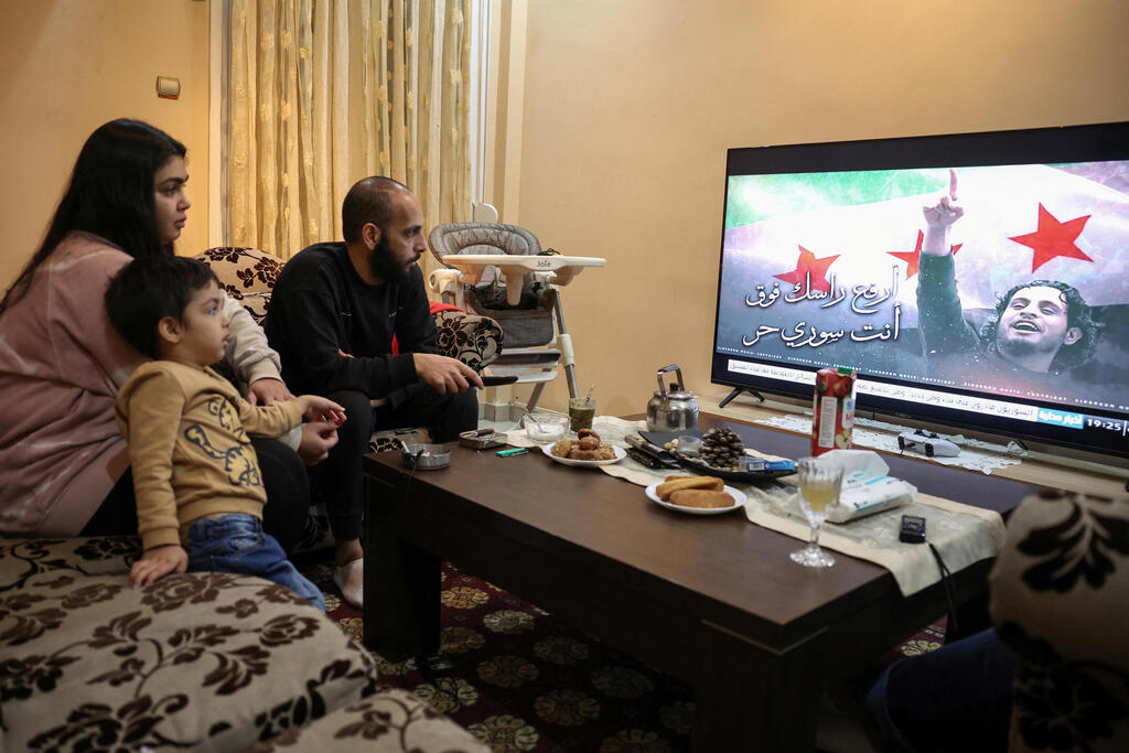Najem Al Moussa, his wife Bushra Al Bukaai, and their youngest son watch news on the events in Syria in their apartment in Athens
