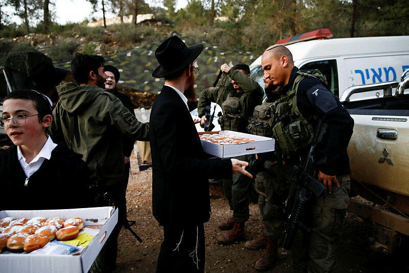 Israeli soldiers receive donuts as they celebrate the first day of Hanukkah, near the Israeli-Lebanon border