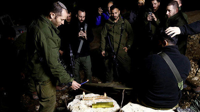 An Israeli soldier lights candles as soldiers gather to celebrate the first day of Hanukkah, near the Israeli-Lebanon border