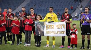 Hapoel Haifa players holding a banner saying "Romi Gonen returns alive" 