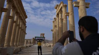 A member of the Syrian Civil Defense (White Helmets) takes a photo of his colleague holding the new Syrian flag at the ancient city of Palmyra, Syria, Saturday