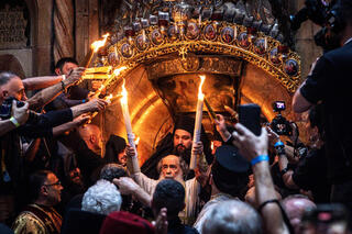 Greek Orthodox Patriarch of Jerusalem Theophilos III, center, transmits fire from candles to believers during the annual Holy Fire ceremony in Jerusalem's Holy Sepulchre church, a day before Orthodox Easter on April 19, 2025 