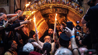 Greek Orthodox Patriarch of Jerusalem Theophilos III, center, transmits fire from candles to believers during the annual Holy Fire ceremony in Jerusalem's Holy Sepulchre church, a day before Orthodox Easter on April 19, 2025 