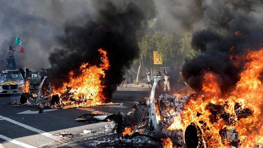 Rioters set cars on fire in Los Angeles (Photo: Mario Tama / Getty Images North America / AFP) ארה"ב קליפורניה לוס אנג'לס מפגינים שורפים כלי רכב אוטונומיים מהומות בעקבות מעצר מהגרים בלתי חוקיים
