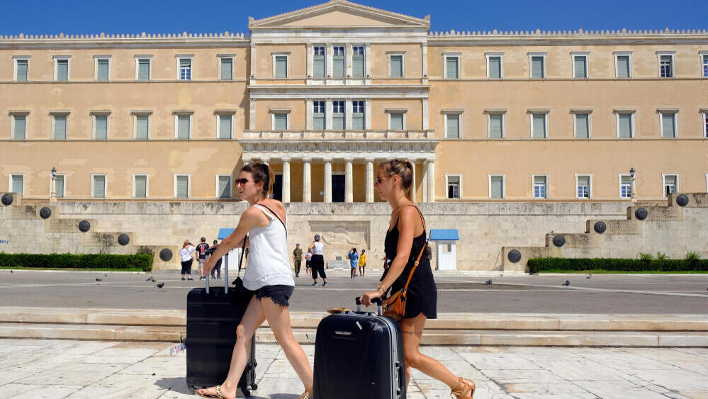 תיירות עם מזוודות מול בניין הפרלמנט באתונה