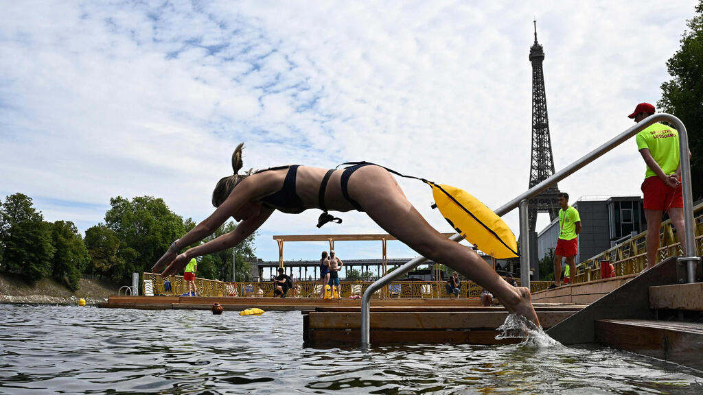 Jumping into the river with the Eiffel Tower in the background (Photo: JULIEN DE ROSA / AFP) אישה קופצת למים באתר הרחצה הבטוח גרנל שעל נהר הסן