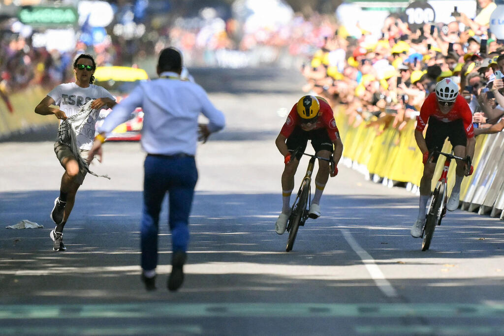 A security officer rushes to intercept a pro-Palestinian protester who stormed the course near the finish line of Stage 11 of the Tour de France in Toulouse, France, Wednesday, July 17, 2025. The demonstrator, wearing a shirt reading 'Israel out of the Tour,' disrupted the final sprint between Norway’s Jonas Abrahamsen, center, and Switzerland’s Mauro Schmid, right, before being subdued (Photo: Marco BERTORELLO / AFP) המפגין הפרו-פלסטיני במהלך הטור