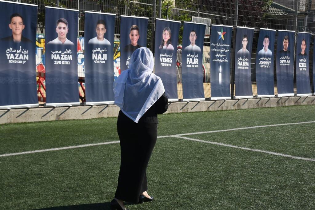 A woman stands before banners bearing the names and faces of 12 children killed in a Hezbollah rocket strike, during a memorial ceremony marking one year since the attack, at a soccer field in Majdal Shams in northern Israel, Sunday, July 27, 2025 (Photo: Avihu Shapira) טקס אזכרה לזכר האסון במג׳דל שאמס
