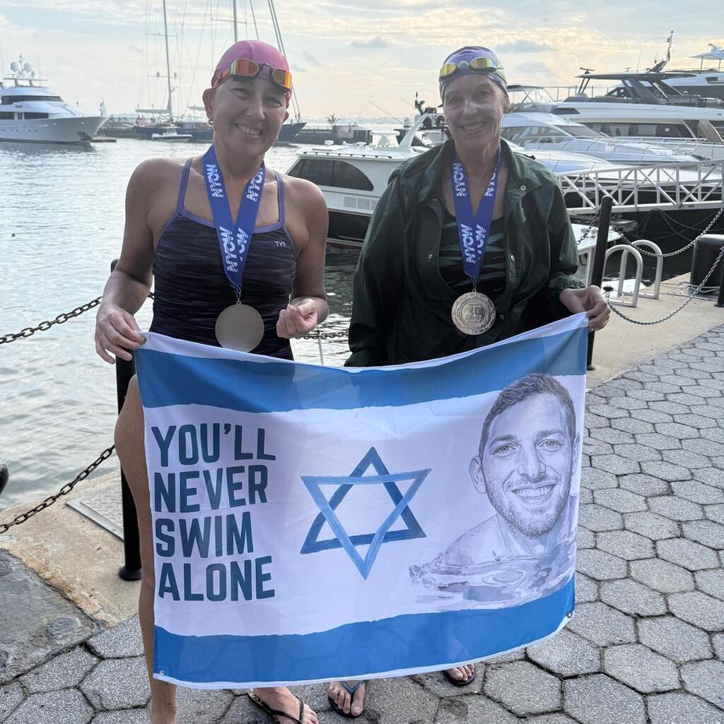 Debbie (right) with her swimming partner Anat Achimeir Eshchar, holding a flag with Yaron’s photo; 'Yaron is always with me'