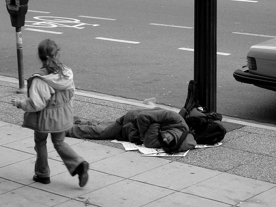 A child walks past a man sleeping on the sidewalk, Canada