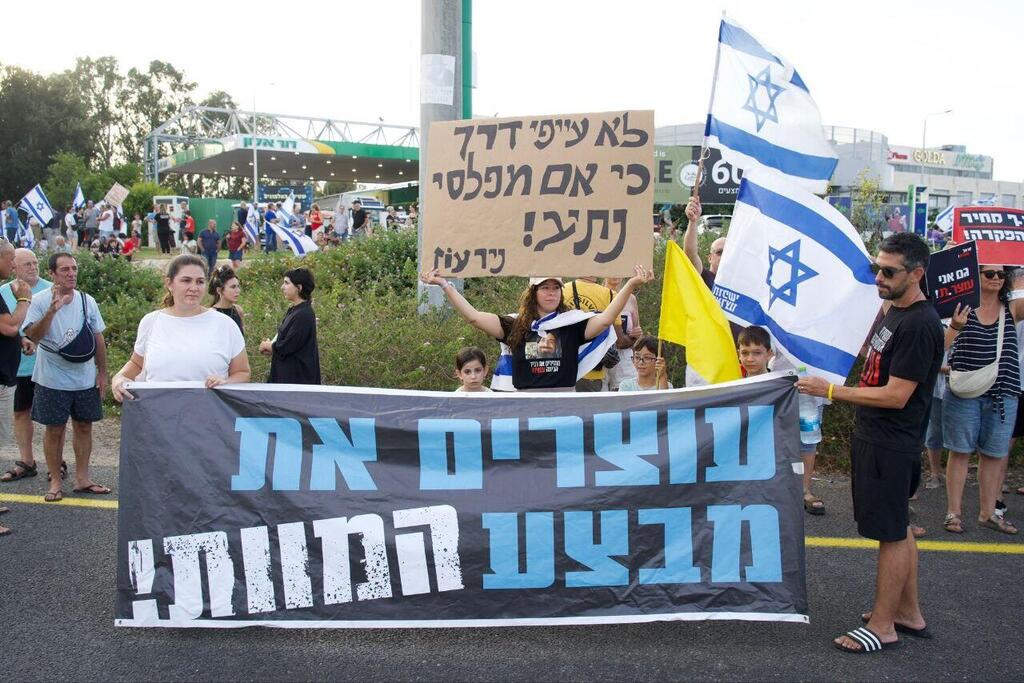 Protesters hold signs and Israeli flags during a demonstration against the expansion of the war in Gaza and in support of a hostage release deal, near Tel Aviv, Israel, Sunday, Aug. 17, 2025 (Photo: Tal Guterman) הפגנת "יום עצירה" בצומת העוגן