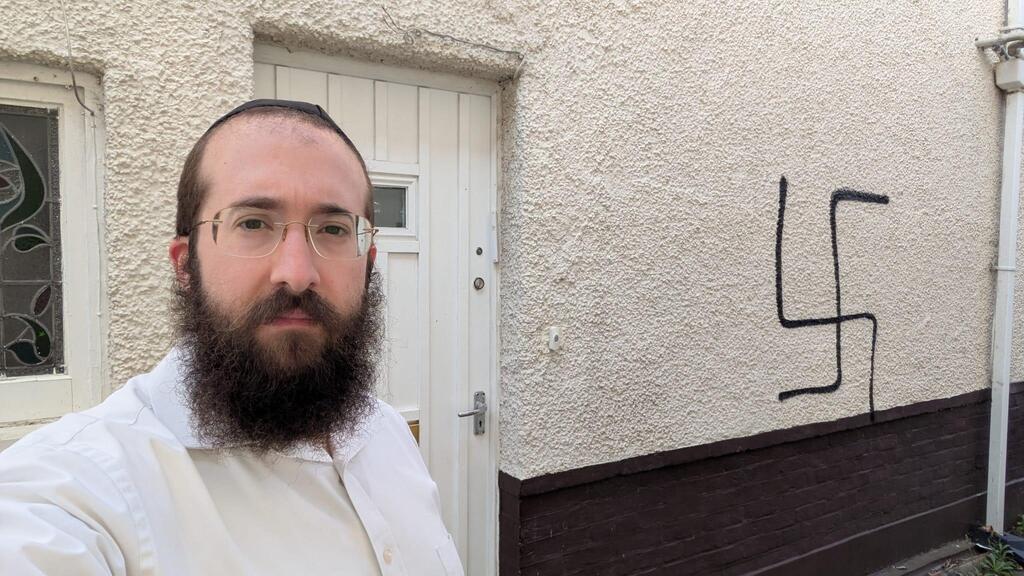 הרב בנצי אלפרוביץ' לצד הגרפיטי של צלב קרס שרוסס על ביתו