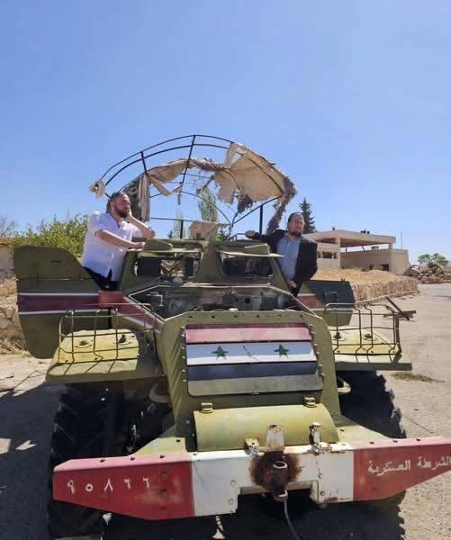 Moshe Klein (right) and his friend seen standing on a military vehicle flying the flag of Syria’s former regime הרב משה קליין בביקורו בדמשק