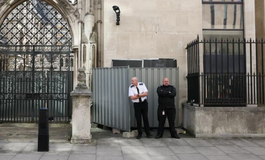 Security guards stand in front a screen covering a new mural by anonymous artist Banksy on the Royal Courts of Justice in London 