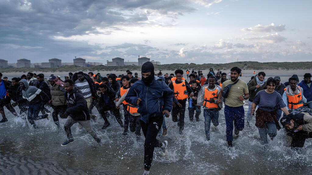 מהגרים רצים בניסיון לעלות על סירה ב חוף ב צרפת באזור גרבלין ליד קאלה לפני חציית תעלמת למאנש לכיוון אנגליה בריטניה 12 באוגוסט