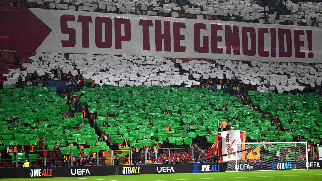 אוהדי גלאטסראיי עם תפאורה של דגל פלסטין ושלט נגד ישראל
