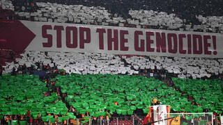 אוהדי גלאטסראיי עם תפאורה של דגל פלסטין ושלט נגד ישראל