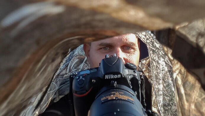 צלם הטבע יוסי מלכא בעת תצפית מוסווית בשטח. רשת ההסוואה מאפשרת לצלמים להיטמע בטבע ולצלם מבלי להפריע לבעלי החיים