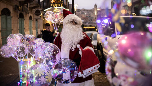 A man dressed as Santa Claus sells balloons near Nativity Square during a Christmas tree lighting ceremony in Bethlehem, West Bank, on December 6, 2025 