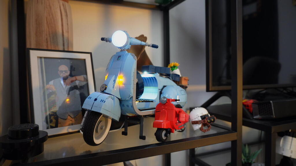 A detailed Lego model of a blue Vespa scooter, illuminated with custom lights, sits on a display shelf in the home of Lego collector Gal Zahavi 