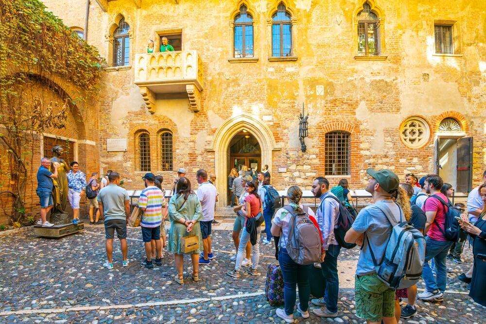 תיירים עומדים בתור מתחת למרפסת של יוליה בחצר Casa di Giulietta (בית יוליה), וממתינים להצטלם לצד פסל יוליה