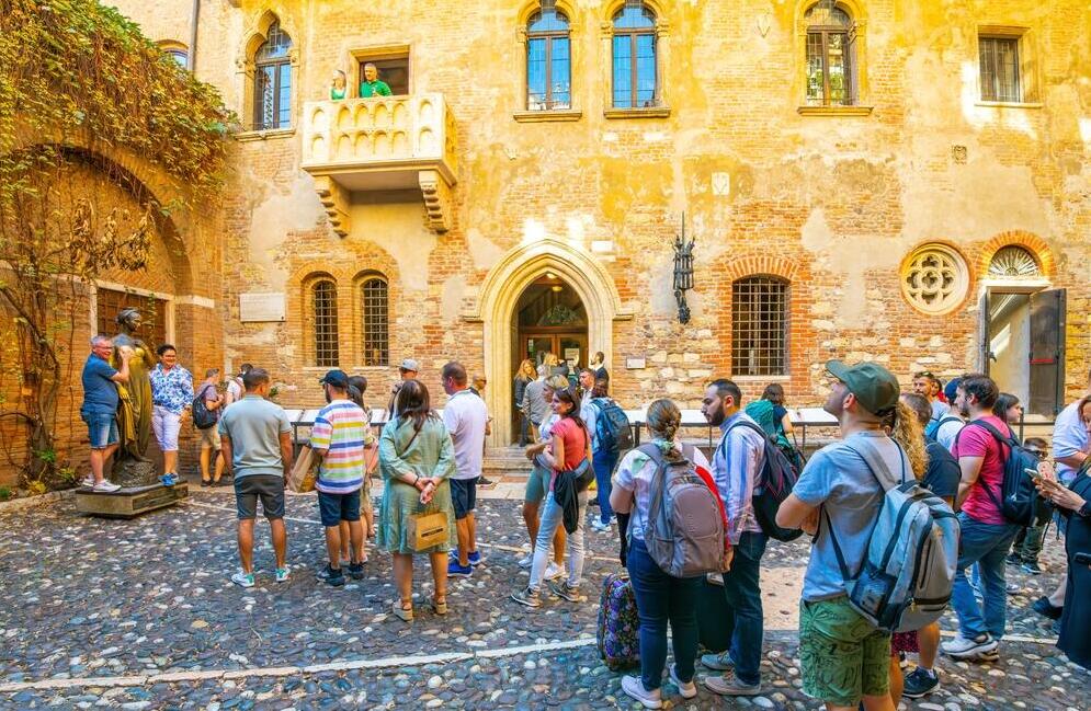 תיירים עומדים בתור מתחת למרפסת של יוליה בחצר Casa di Giulietta (בית יוליה), וממתינים להצטלם לצד פסל יוליה