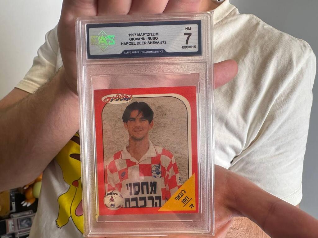 Dor holds a graded 1997 Giovanni Russo soccer sticker from the Israeli Maftzim collection, part of his efforts to preserve local collectibles overlooked by global grading companies 