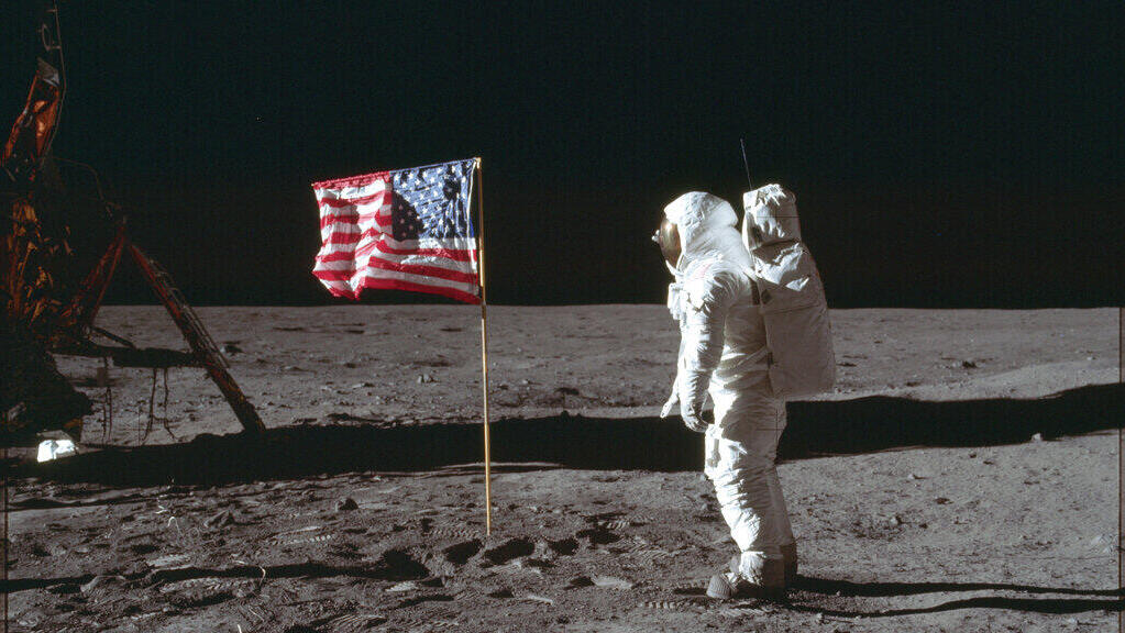 האסטרונאוט באז אולדרין, הולך על הירח, לצד דגל ארצות הברית, כחלק ממשימת אפולו 11 בשנת 1969