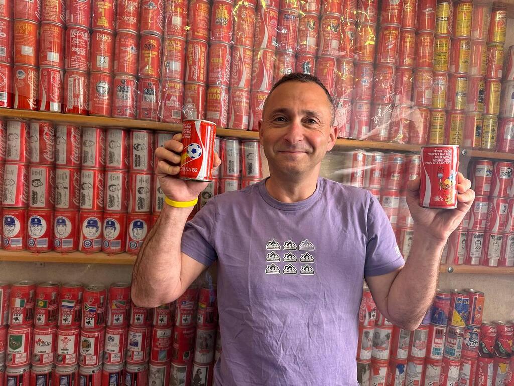 Coca-Cola can collector Ophir holds two rare cans from his collection at his home in Kibbutz Tzora, Israel, Sunday, Dec. 29, 2025. Behind him are hundreds of vintage cans arranged by theme, country and campaign 