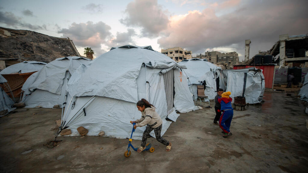 ילדים משחקים במחנה אוהלים לפלסטינים עקורים במחנה הפליטים ג’באליה שבעיר עזה, 6 בפברואר 2025, לאחר שאספו מזון שנתרם.
