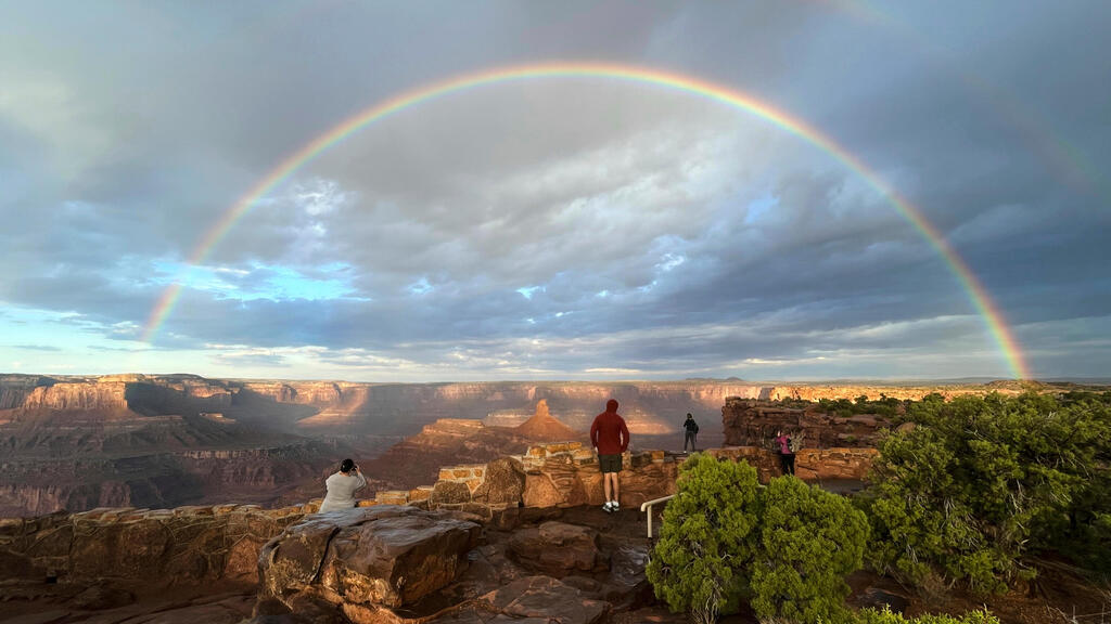 אנשים מתכנסים בנקודת תצפית כאשר קשת כפולה מופיעה מעל פארק המדינה דד הורס פוינט, סמוך למואב שבמדינת יוטה, לאחר הזריחה ובעקבות סופת רעמים, 9 באוקטובר 2025.