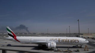 מטוסים של אמירייטס בנמל התעופה בדובאי על רקע תימרות עשן ממתקפה איראנית, אתמול