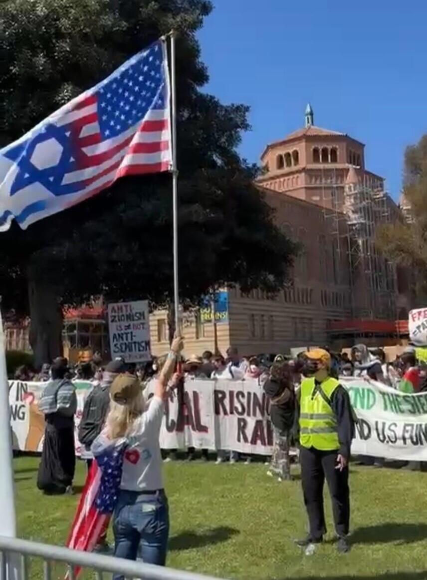 Aya Shechter with an American and Israeli flag at UCLA stands alone against anti-Israel demonstrators during a permitted pro-Israel rally