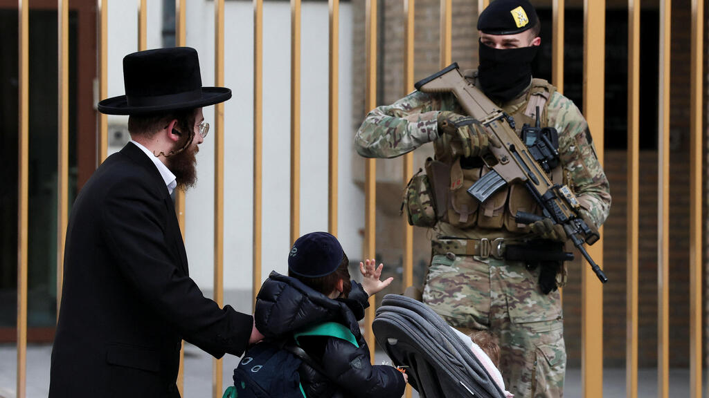 ילד מנוף לשלום לאחד החיילים החמושים שמאבטחים את בתי הכנסת בבלגיה