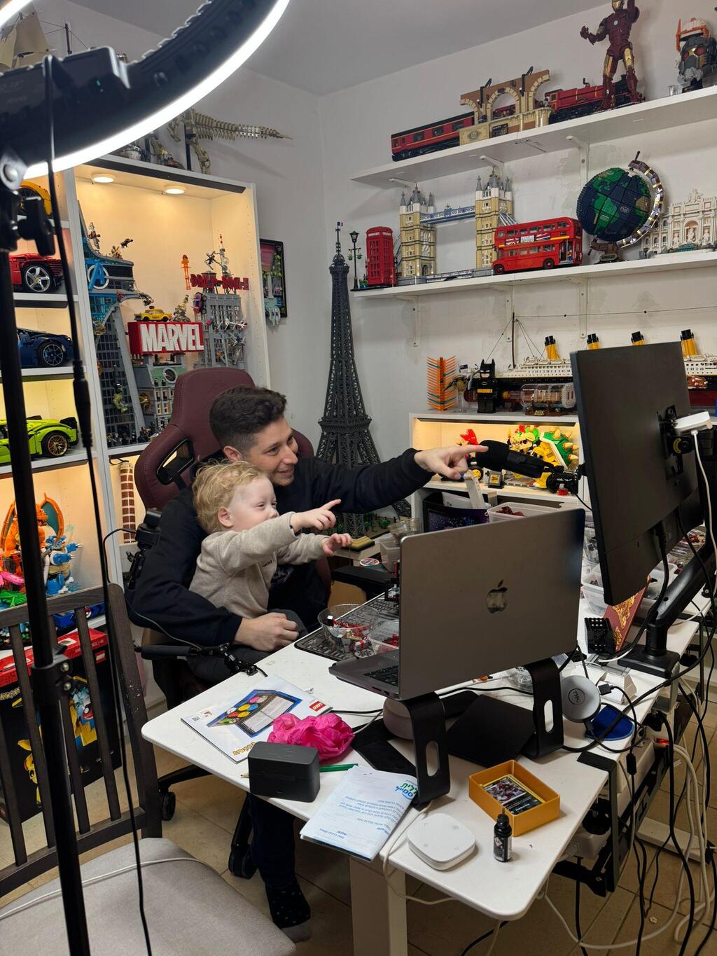 Elliott and his son, AJ, point toward a screen in Elliott’s LEGO studio, where he began livestreaming builds during AJ’s treatment for a rare brain tumor (Photo: Courtesy) Elliott and his son, AJ, point toward a screen in Elliott’s LEGO studio, where he began livestreaming builds during AJ’s treatment for a rare brain tumor