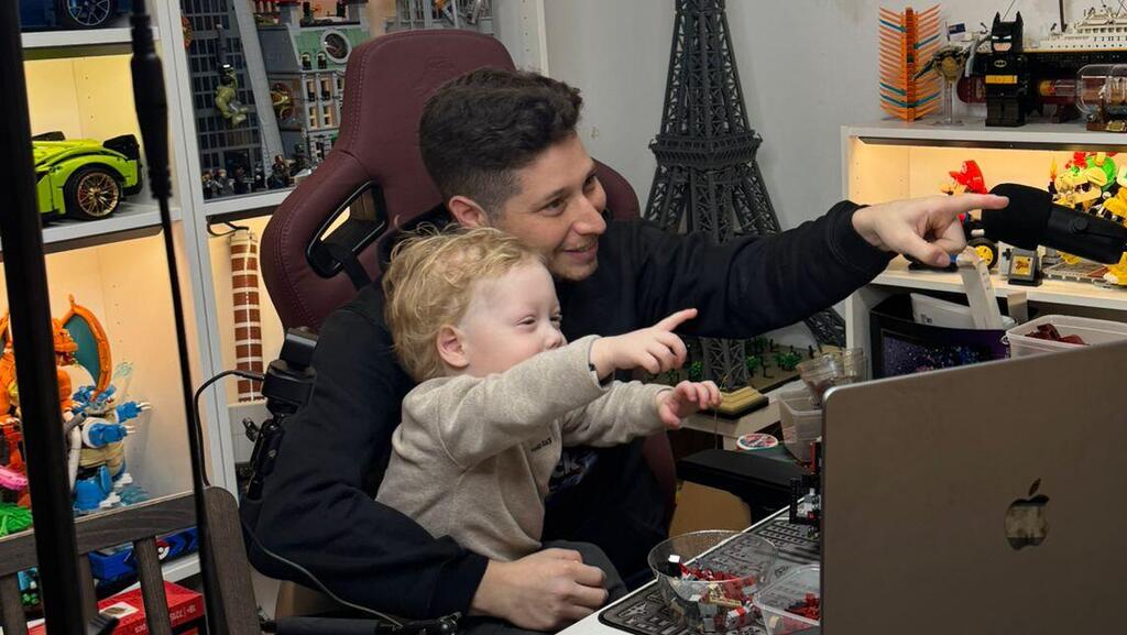 Elliott and his son, AJ, point toward a screen in Elliott’s LEGO studio, where he began livestreaming builds during AJ’s treatment for a rare brain tumor 