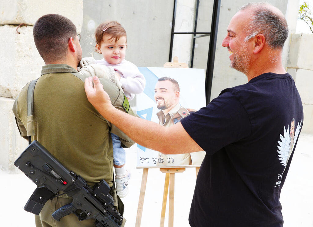 רס"ן ר' עם התינוקת רון והאב השכול רוני פרץ, על רקע תמונתו של רז ז"ל