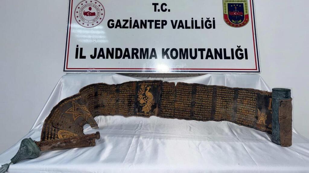 כתב היד העברי החקוק באותיות זהב על עור פיתון, מוצג לצד מעטפת הנחושת המעוטרת שלו