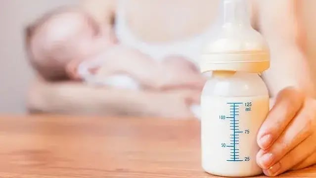 Illustrative: A mother holds a baby, with a bottle of breast milk at foreground 