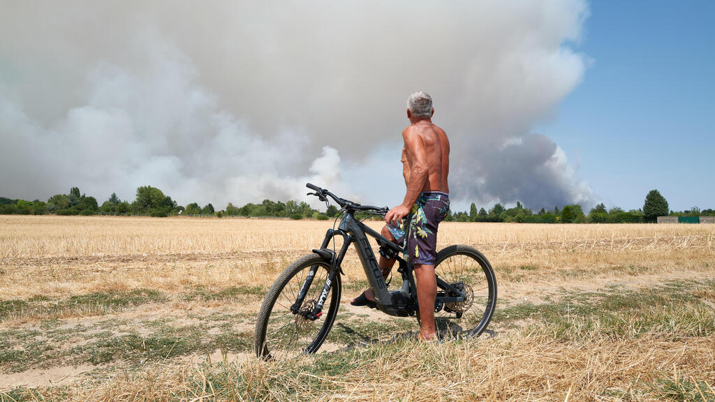 A cyclist watches smoke rise as additional fires force road closures, including the A6 between Paris and Lyon (Photo: Pierre Crom/Getty Images) מזג אוויר גל חום צרפת שריפה ליד פריז
