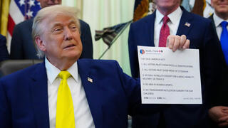  Trump shows reporters at the White House a printout of one of his Truth Social posts in June 