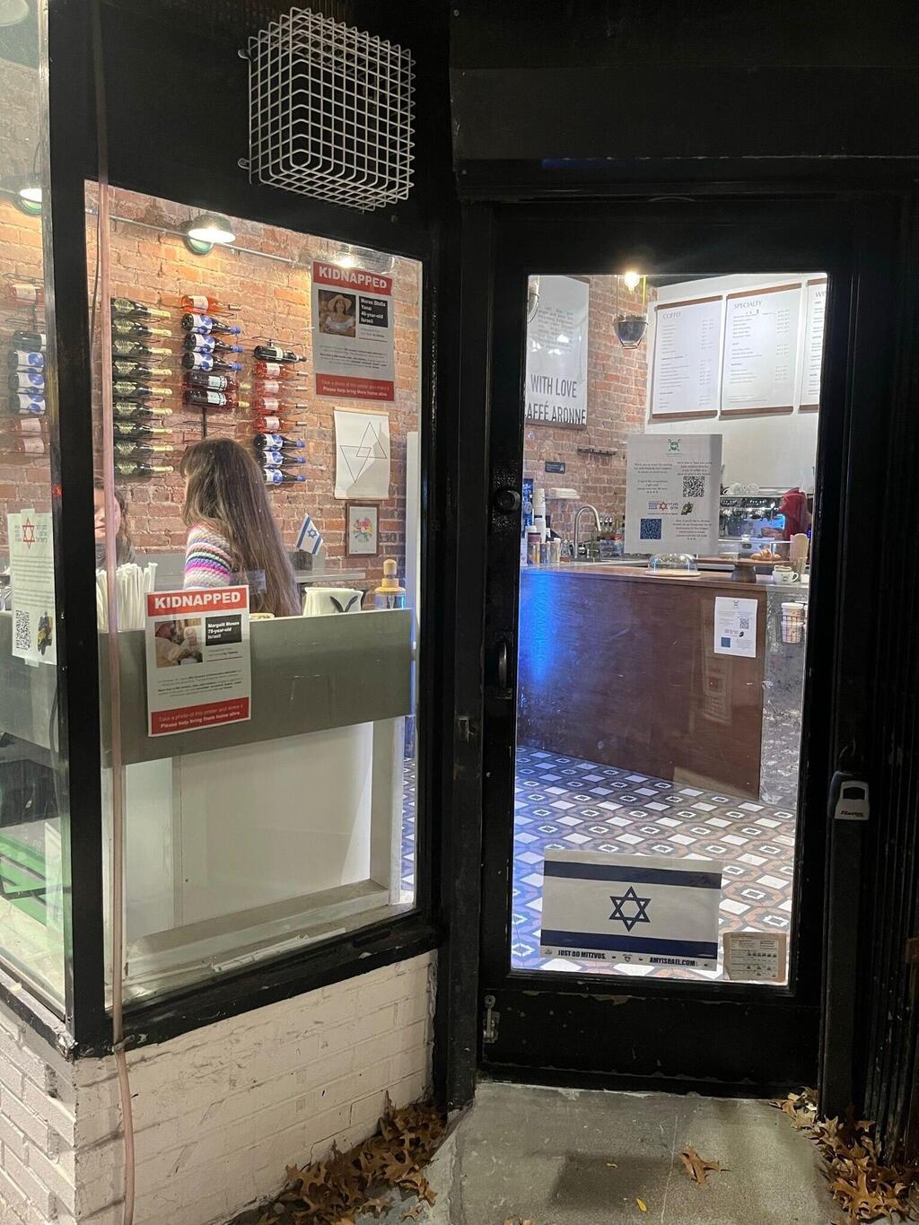 Caffè Aronne; an Israeli flag and a hostage poster, placed behind the window so they could not be torn down (Photo: Aaron Dahan) קפה ארון